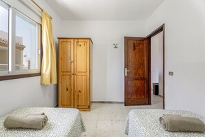 Une chambre avec deux lits, une armoire en bois, une porte et une fenêtre avec un rideau.