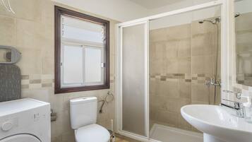 Ein Badezimmer mit Toilette, Waschmaschine, Duschkabine und Waschbecken.