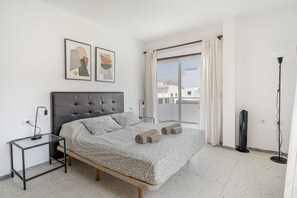 Ein Schlafzimmer mit Bett, Nachttisch, Stehlampe und Blick auf die Stadt durch das Fenster.