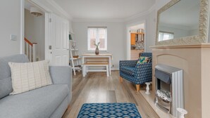 Uma sala de estar com um sofá cinza, uma poltrona azul estampada, uma mesa de centro branca e uma lareira.