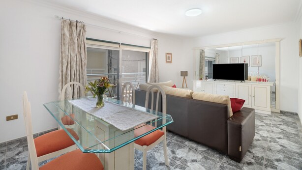 Una sala de estar moderna con una mesa de comedor de vidrio, un sofá y un televisor al fondo.