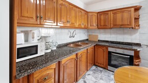 Una cocina con armarios de madera, encimera de granito, microondas, cafetera, lavabo y horno.