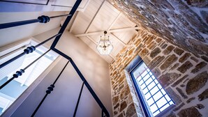 Ein Zimmer mit hohen Decken, Steinwänden, einem Chandelier und einem fenster mit Gittermuster.