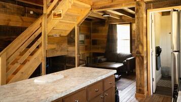 A rustic cabin interior with a kitchen area, wooden walls, a staircase, and a cozy seating area.