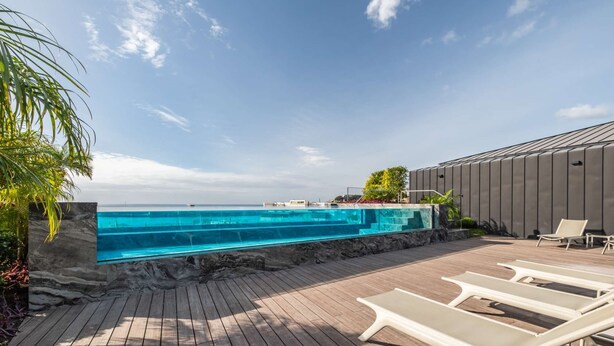 Une piscine à l’eau claire, une terrasse en bois et des chaises longues.