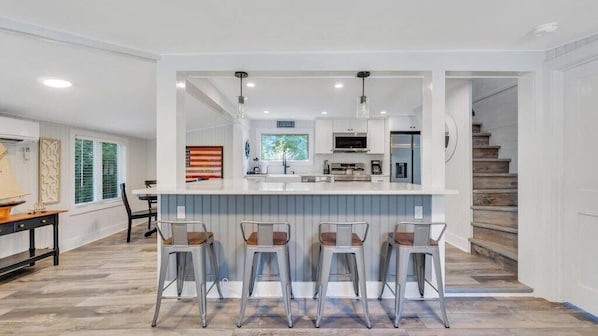 A modern kitchen with a central island, bar stools, and a staircase leading to another level.