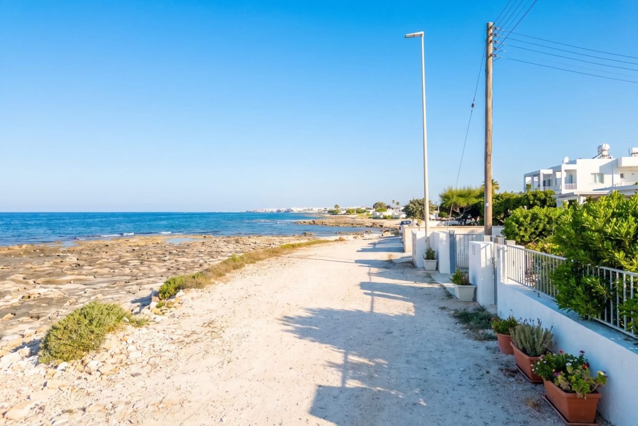 Un paseo marítimo con vistas despejadas al mar, un sendero arenoso y edificios blancos con balcones.