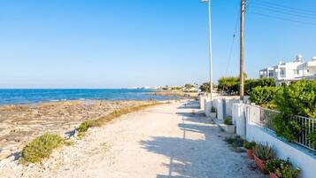 Un paseo marítimo con vistas despejadas al mar, un sendero arenoso y edificios blancos con balcones.