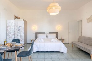 Ein Hotelzimmer mit einem Bett, einem Esstisch mit Stühlen, einer Couch, einer Hängelampe und einer Wand mit dekorativen Tellern.