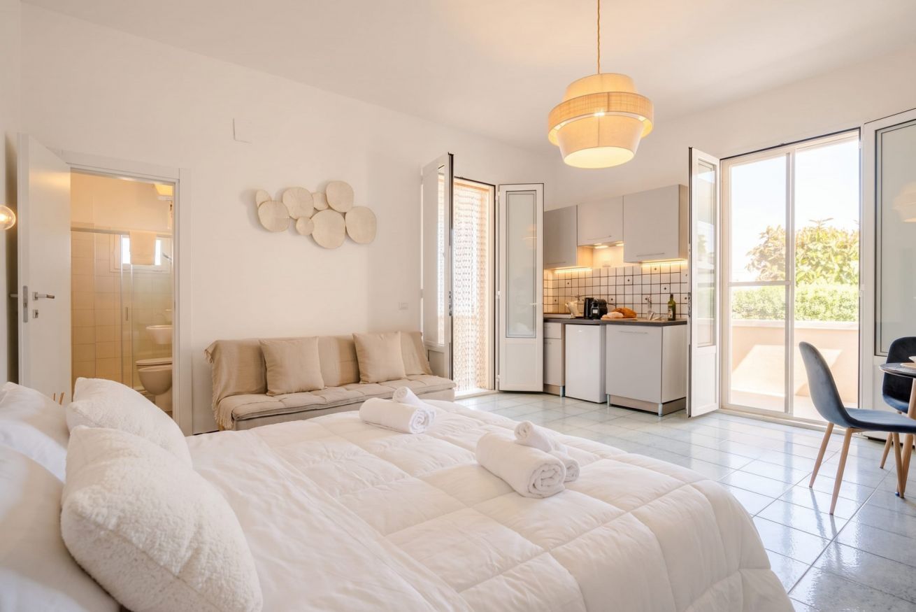 A modern hotel room with a large bed, a sofa, a dining area, and a view of the outdoors.