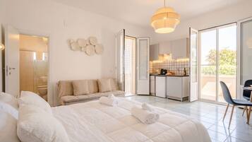 A modern hotel room with a large bed, a sofa, a dining area, and a view of the outdoors.