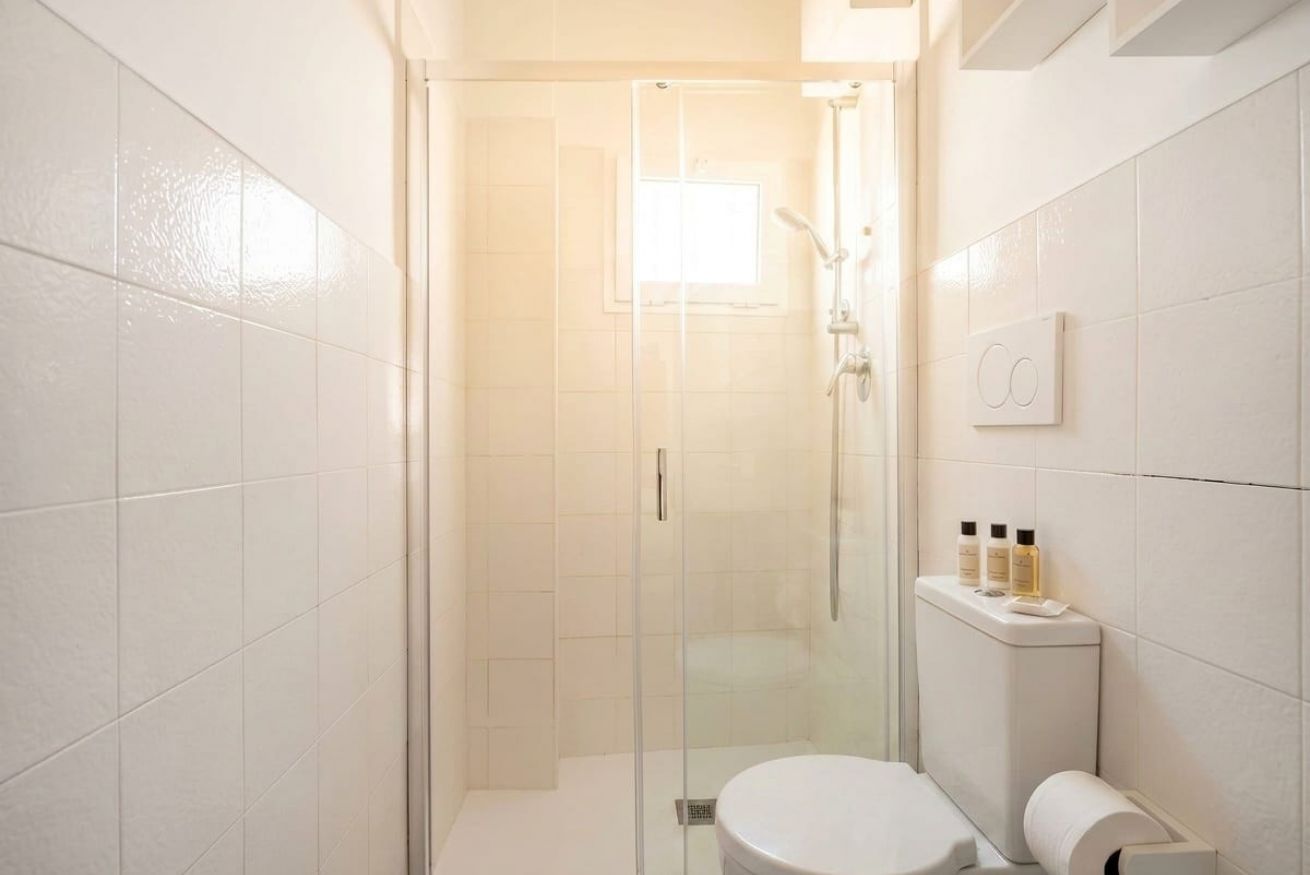 Un baño con ducha de vidrio, un inodoro y un pequeño estante con artículos de aseo.