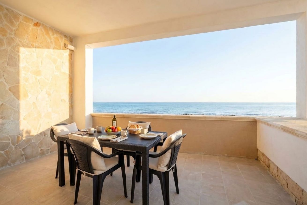 A balcony with a table set for dining, overlooking the sea.