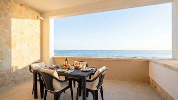 A balcony with a table set for dining, overlooking the sea.