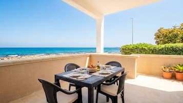 A terrace with a table set for dining, overlooking a beach.