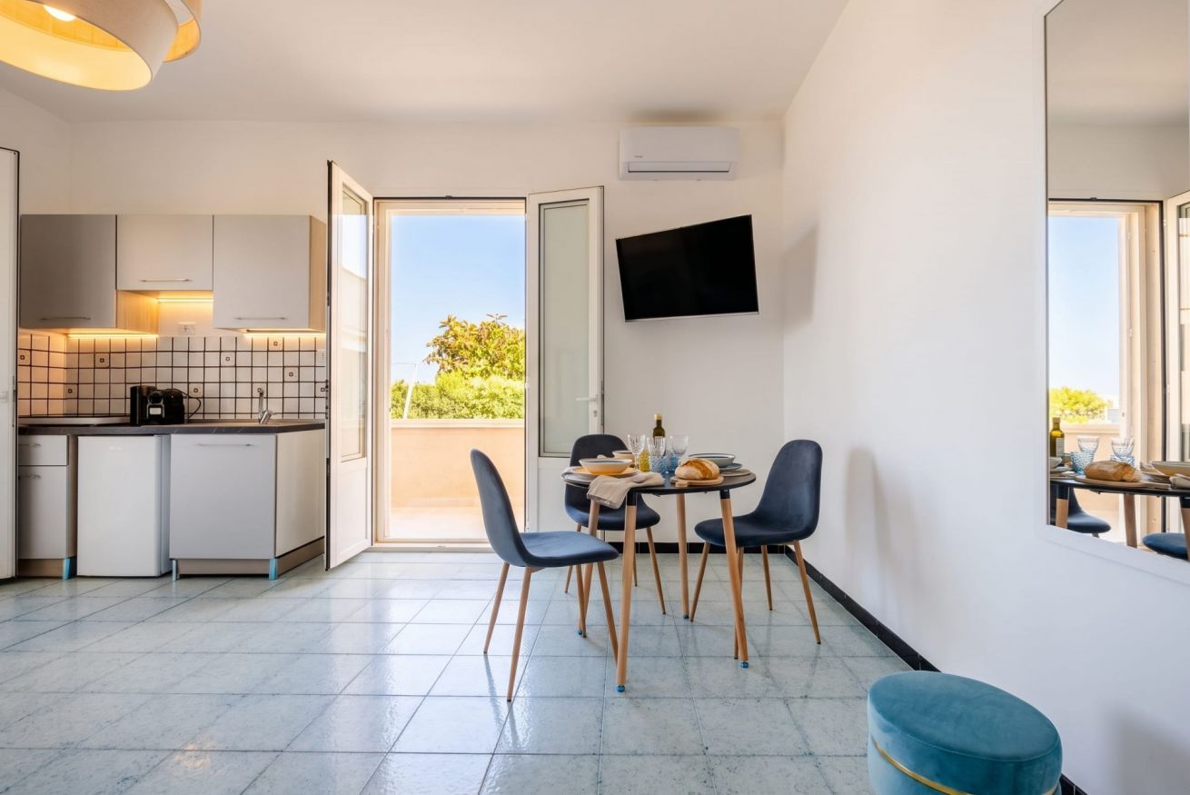 A modern kitchen with a dining area, a flat-screen TV, and a view of greenery outside.