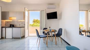 A modern kitchen with a dining area, a flat-screen TV, and a view of greenery outside.