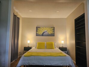 A bedroom with a bed, two bedside lamps, a painting on the wall, and a window with curtains. - Awesome 3-bedroom house with AC in delightful Des Moines (Des Moines)