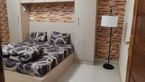 A bedroom with a bed, a wardrobe, a lamp, and a brick-patterned wall.