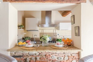 A kitchen with a stone countertop, a stainless steel range hood, and various fruits and flowers on the counter. - Casa Battisti in Lucca (Lucca)