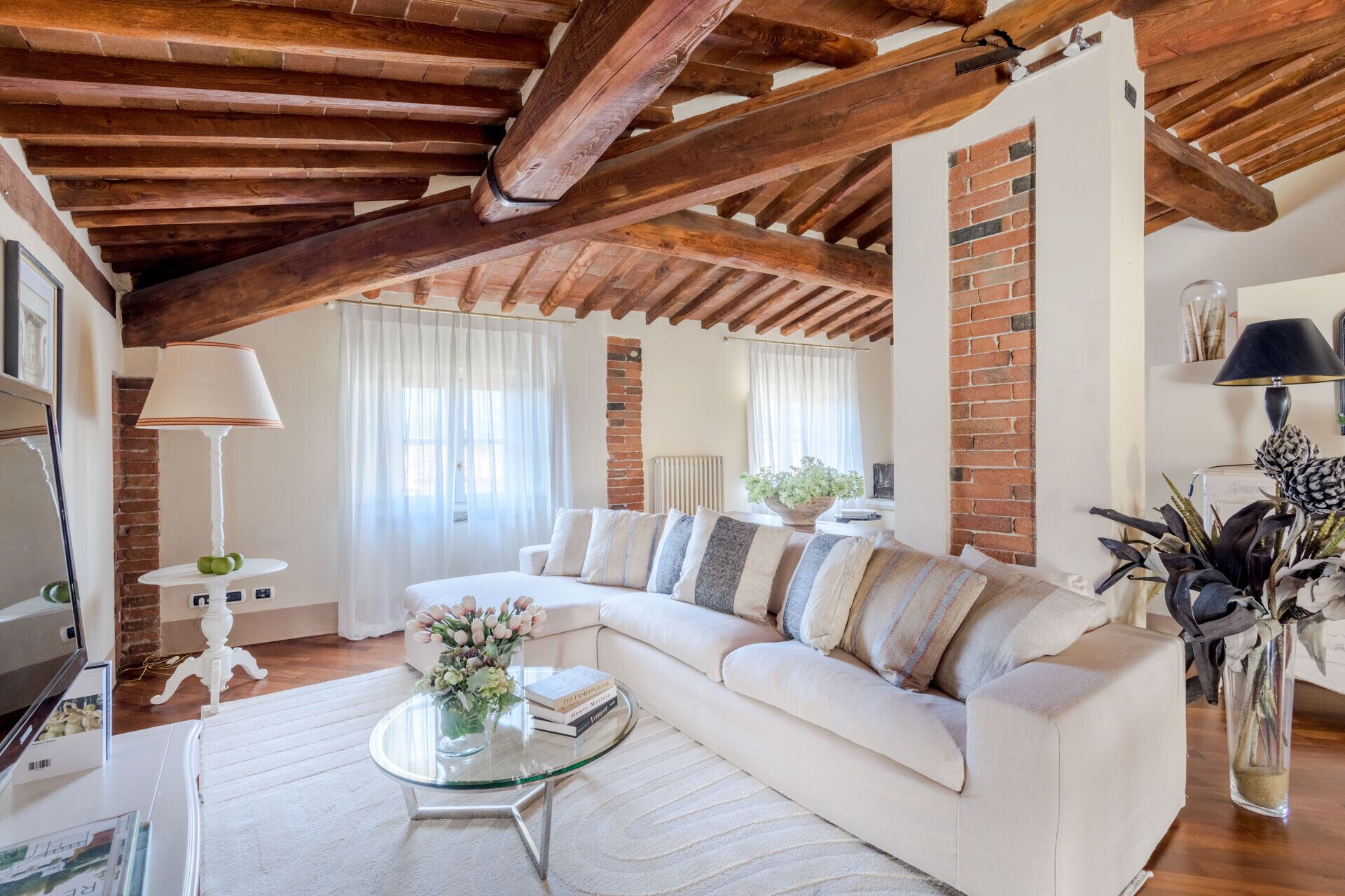 A living room with a white sofa, a glass coffee table, a lamp, and a brick wall.
