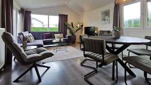 En moderne stue med sofa, stole, spisebord og fjernsyn.
