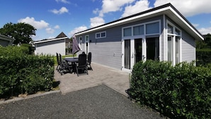 Et moderne etplanshus med en patio, et spisebord med stole, og et overdækket udendørs siddeområde.