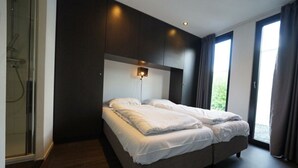 A modern bedroom with a large bed, a walk-in shower, and a view of greenery outside. - Holiday Home in Halfweg With Terrace (Halfweg)