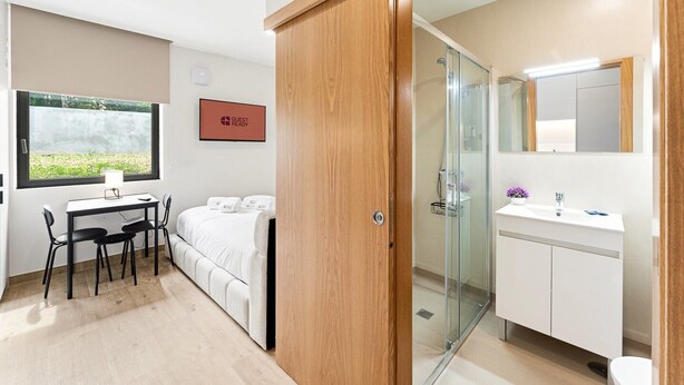 Habitación de hotel con cama, escritorio con sillas, ventana con vistas, baño con espejo y un cartel que dice 'GUEST READY'.