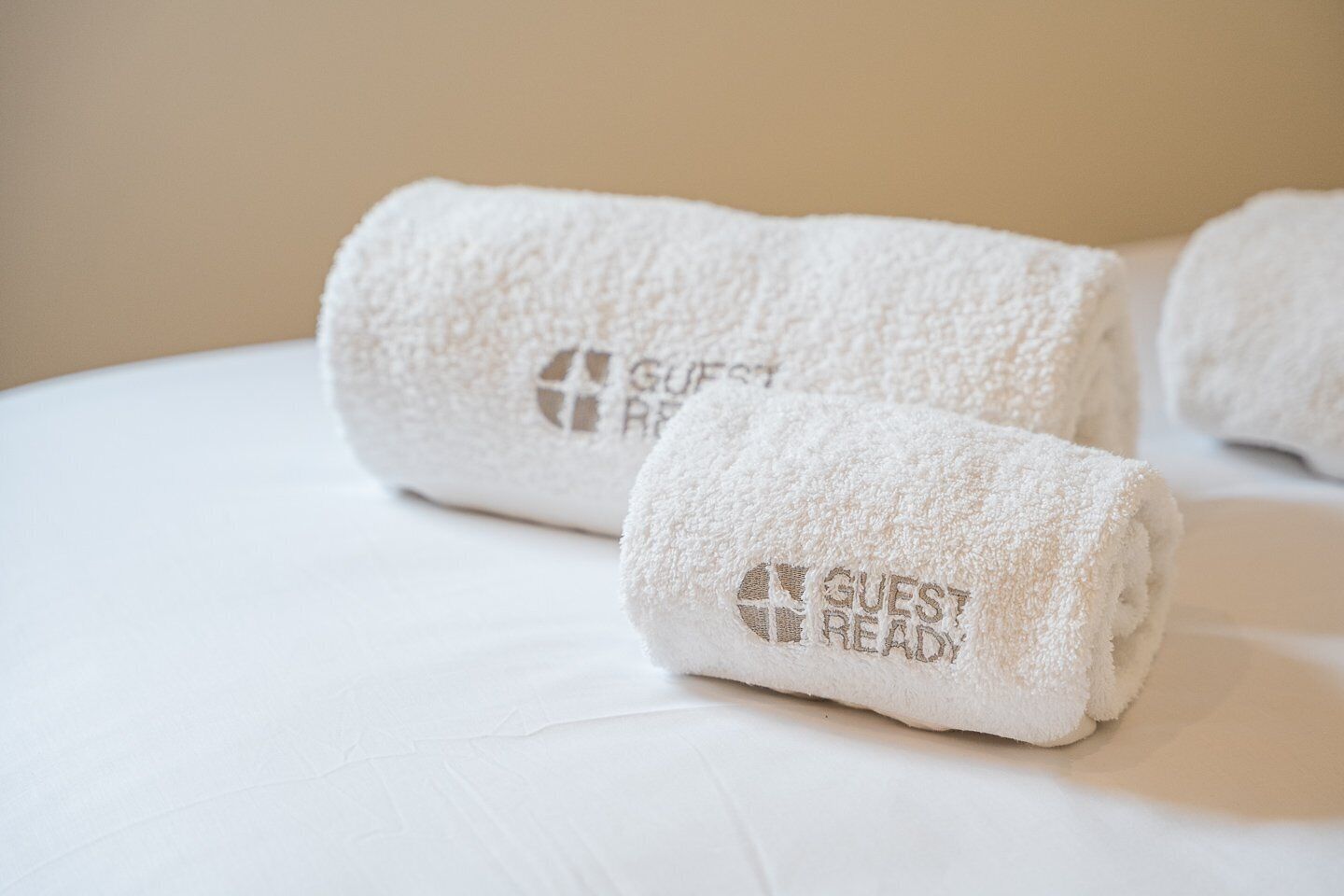 Twee opgerolde witte handdoeken met de tekst 'GUEST READY' op een bed.