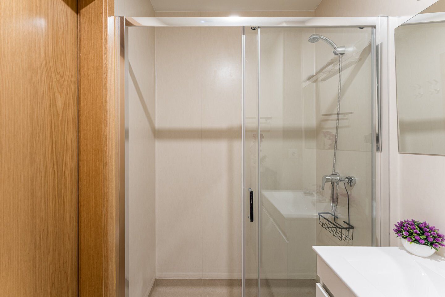 A modern bathroom with a glass shower enclosure, a white sink, and a mirror.