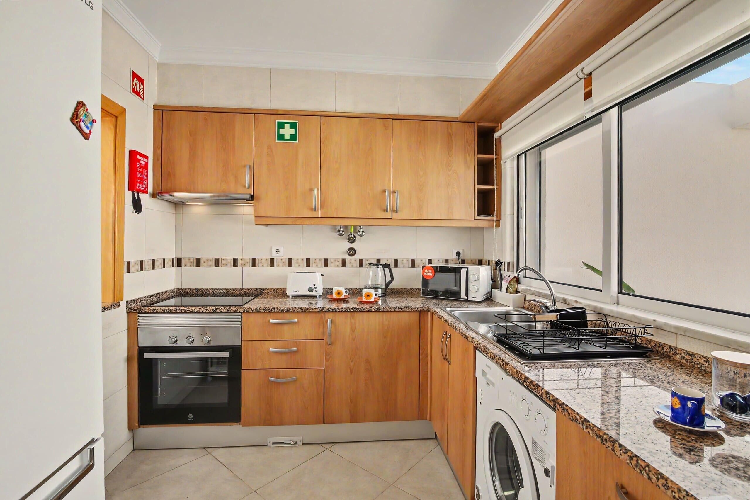 Une cuisine avec des meubles de rangement en bois, un lave-linge, un four à micro-ondes et une cuisinière.