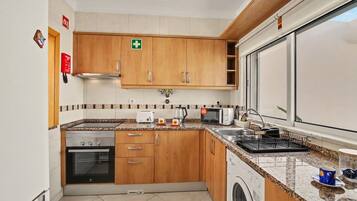 Une cuisine avec des meubles de rangement en bois, un lave-linge, un four à micro-ondes et une cuisinière.