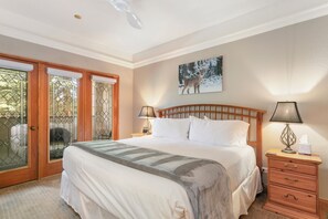 A bedroom with a bed, a nightstand, a lamp, a wooden headboard, a painting, and a sliding glass door. - Charter E160, Beautiful Condo, Pool, Hot Tubs, Spa! (Avon)