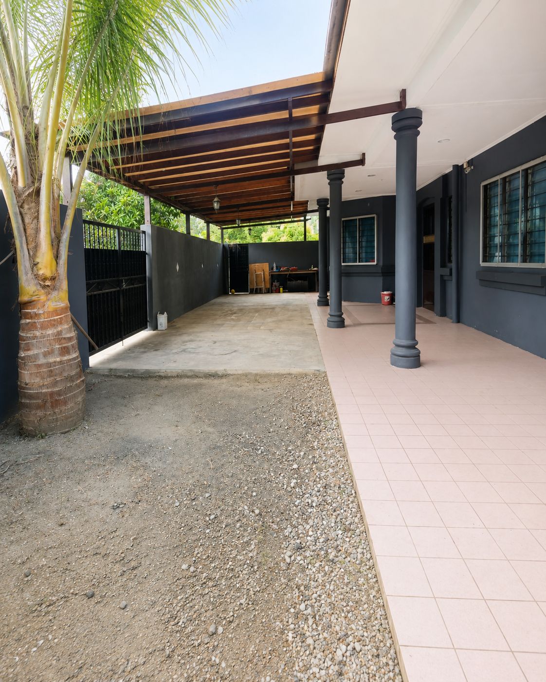 A covered outdoor area with a palm tree, a gravel path, and a tiled walkway.