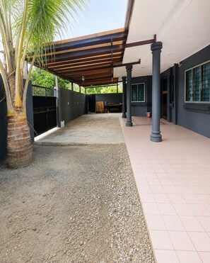 A covered outdoor area with a palm tree, a gravel path, and a tiled walkway.