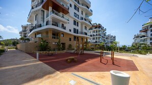 Um edifício residencial com várias andares, varandas, um parquinho e uma área de recreação vermelha.