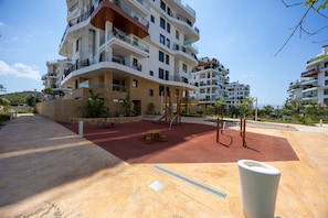 A multi-story residential building with balconies, a playground, and a red play area. - Allonbay Aster 6 - Sea View & Private Jacuzzi (Villajoyosa)