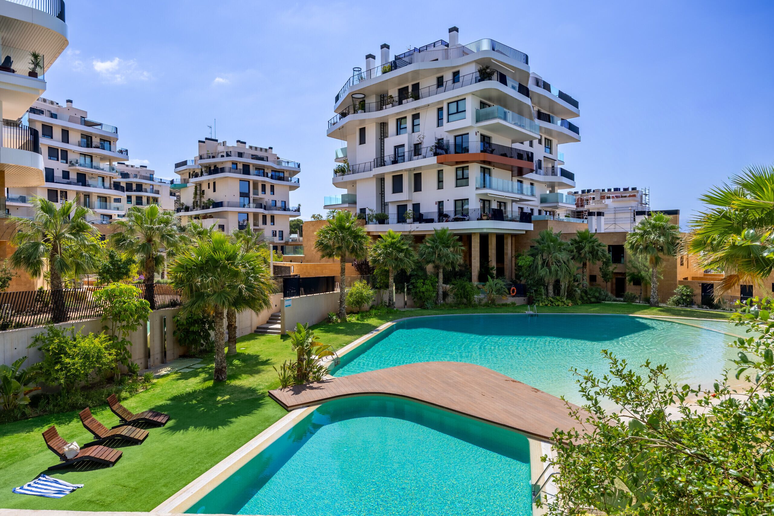 Un moderno complejo residencial con varios edificios de apartamentos, una piscina y abundante vegetación.