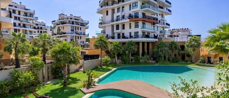 Un moderno complejo residencial con varios edificios de apartamentos, una piscina y abundante vegetación.