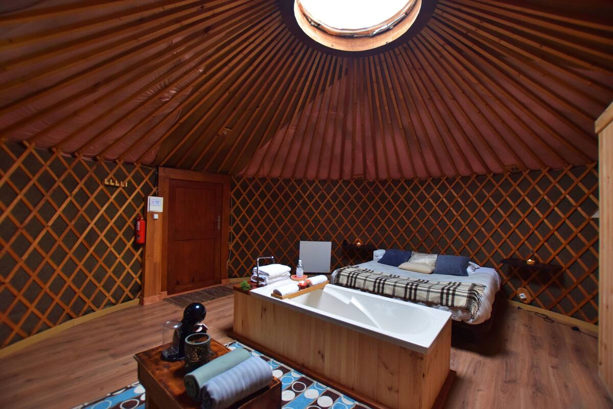 A yurt interior with a bed, wooden floor, and a small desk with a computer.