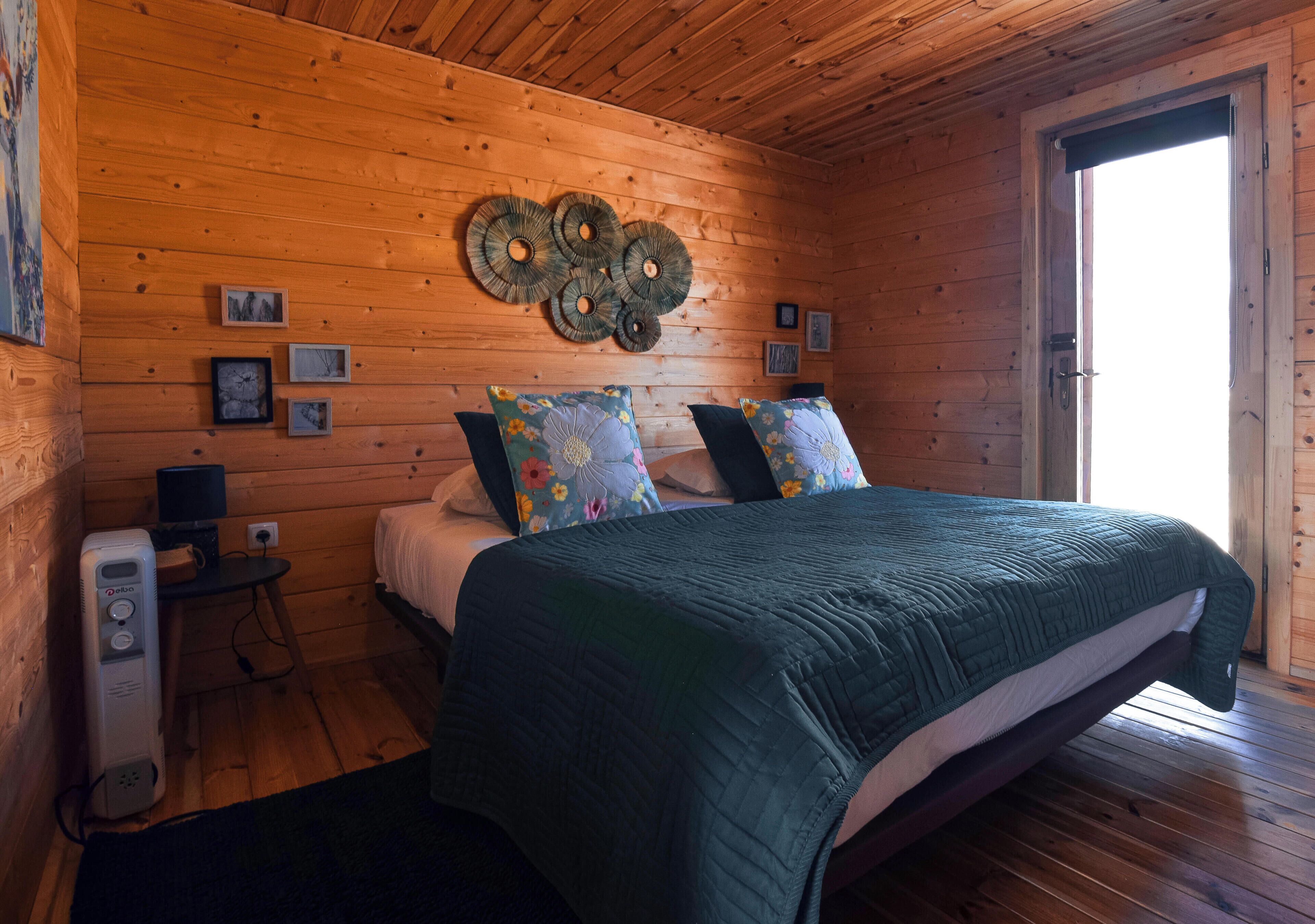 A wooden cabin bedroom with a bed, pillows, a wall clock, and a door.