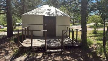 A yurt with a wooden deck and a door, surrounded by trees.