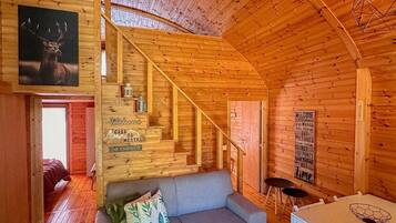 L’intérieur d’un chalet chaleureux, avec un escalier en bois, un canapé, une table et un panneau d’accueil encadré.
