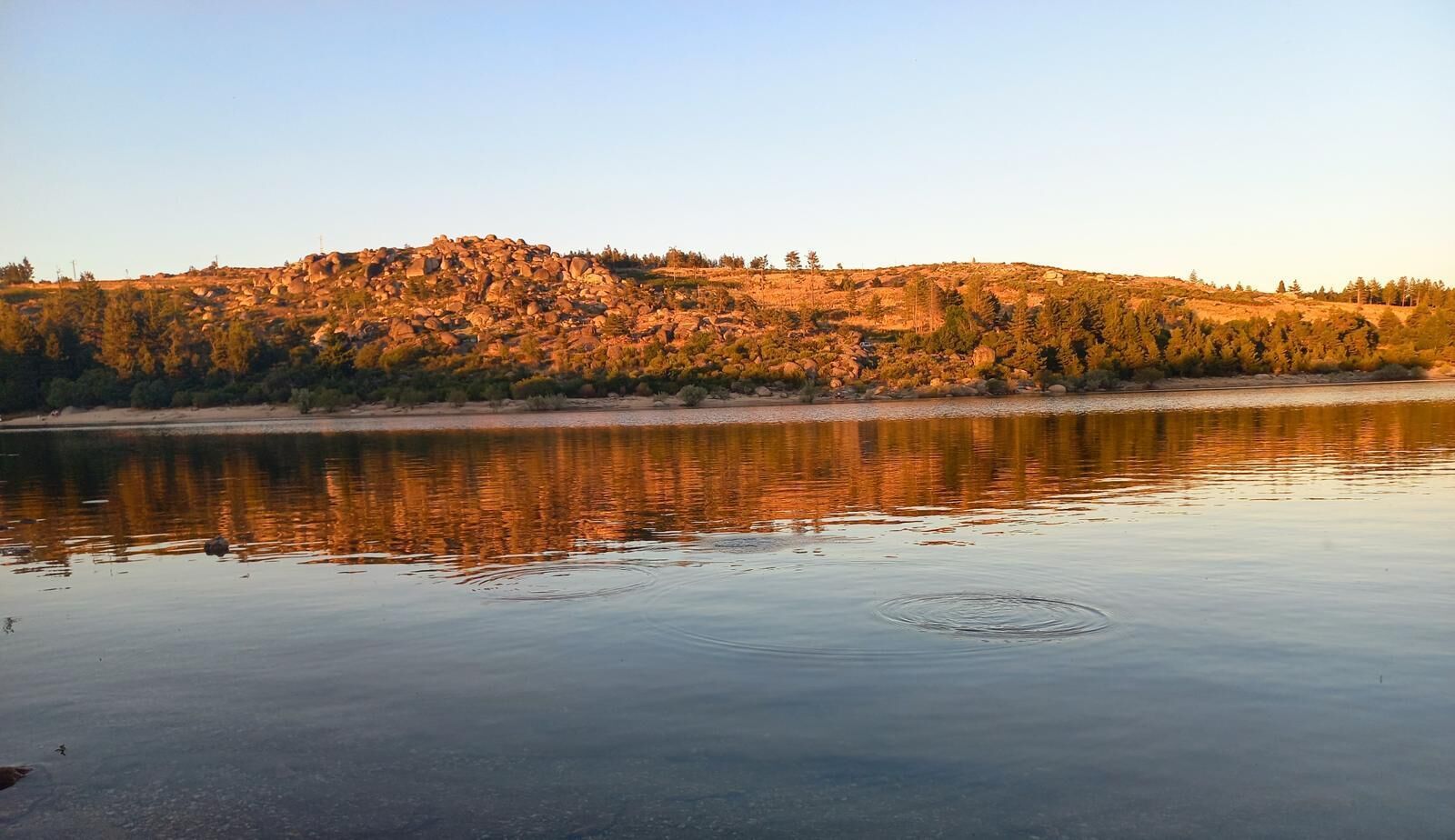 A calm lake with a rocky hill in the background.