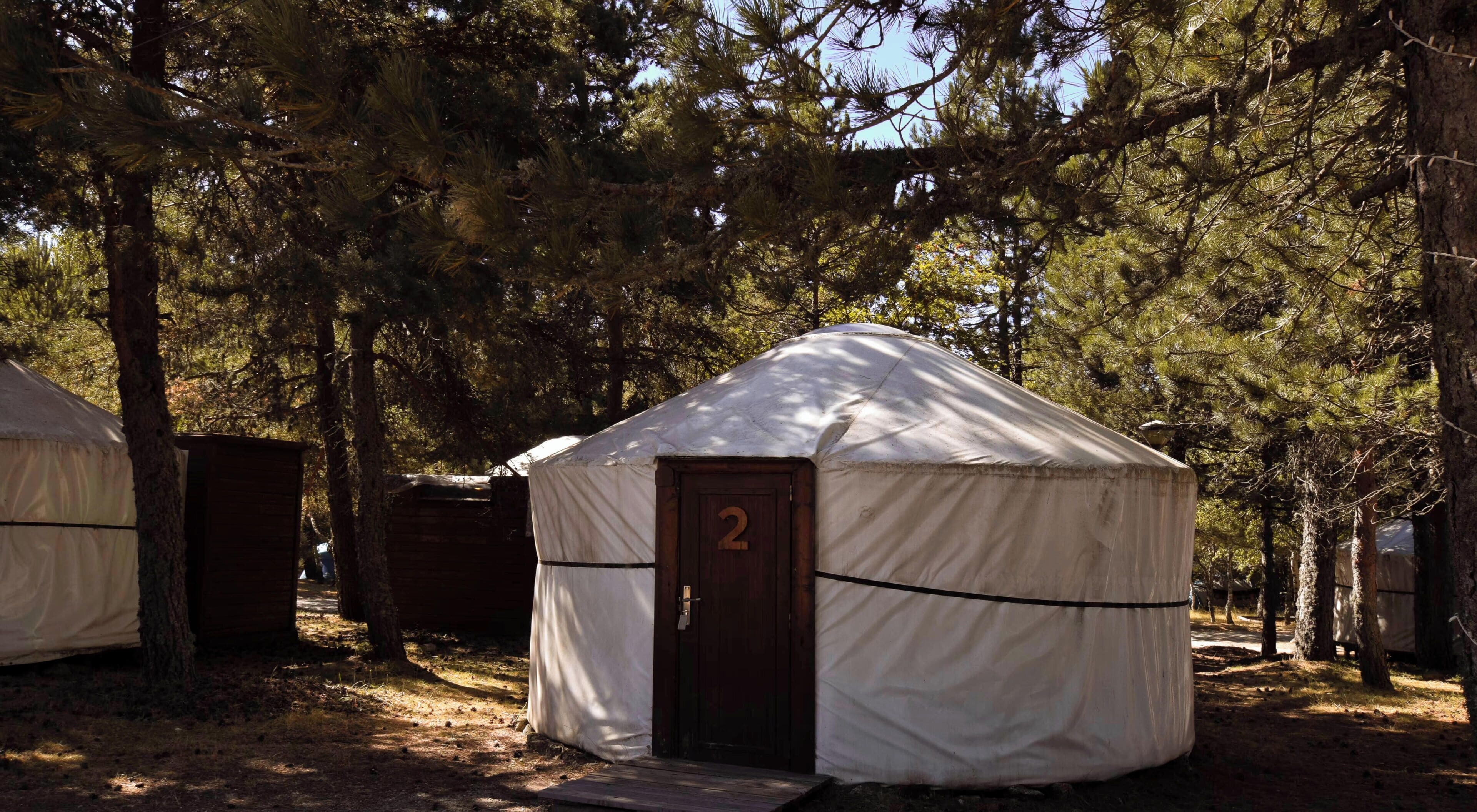 Una yurta con una puerta marcada con el número 2 en una zona boscosa, con otras yurtas al fondo.