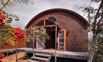 Una cabaña de madera con techo curvo, un porche y una puerta.