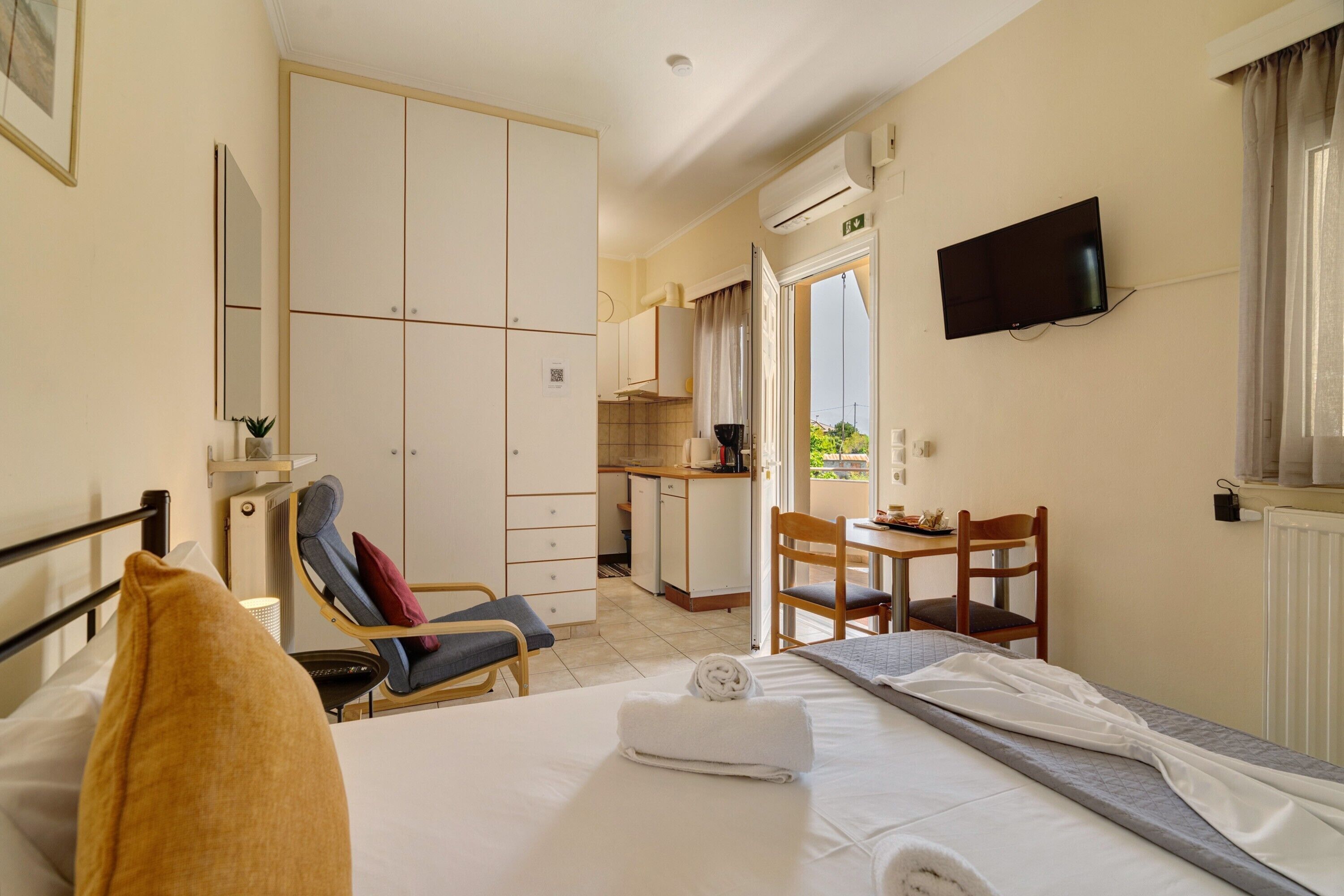 Une chambre d’hôtel comprenant un lit, une chaise, une petite table, un téléviseur et une kitchenette.