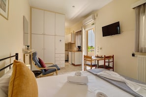 A hotel room with a bed, a chair, a small table, a TV, and a kitchenette.