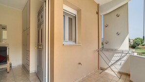 A balcony with a drying rack, a window, and a door leading to a room with a bed and a wardrobe.